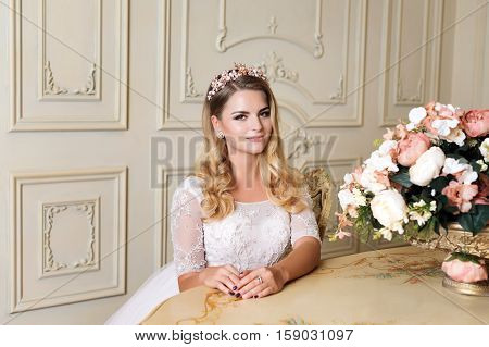 Beautiful blonde woman wearing gorgeous dress and crystal crown posing in luxury classic apartment