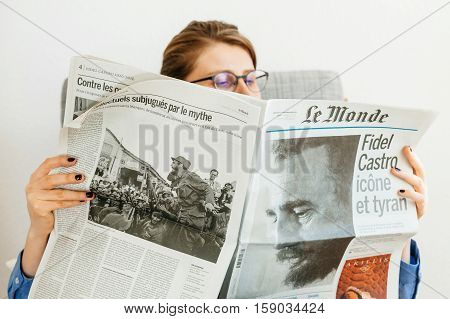 PARIS FRANCE - NOV 29 2016: Woman reading Le Monde newspaper with headline and articles about Fidel Castro Cuban President - dead on November 25 2016