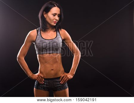 Sports, fitness, athletics concepts. Picture of smiling brunette fitness lady showing her perfect abs and posing with her hands on hips.