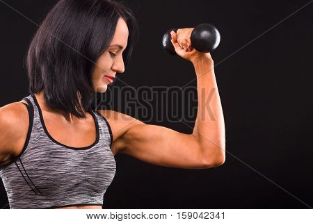Sports and bodybuilding concepts. Profile of fitness woman training with dumbbells. Beautiful lady demonstrating her perfect biceps in studio.