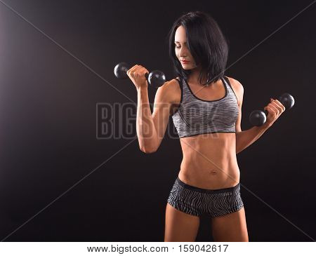 Bodybuilding concept. Sports woman training with dumbbells while demonstrating her muscular body isolated on black in studio.