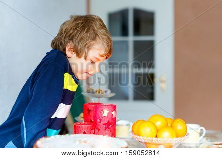 Beautiful little kid boy standing by festive table at Christmas time and holding candle. Excited child celebrating traditional . Xmas party. Catholic and christian celebration in Europe and USA