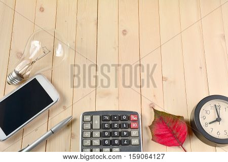 Bulb smart phone silver pen calculator red leaf and clock on the table.