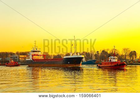 Tugboats assisting cargo ship in port at sunrsie.