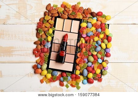 Red lipstick cosmetic powder and mix of dragee with raisins or peanuts inside marmalade or jelly candies almonds on vintage wooden background children`s cosmetic