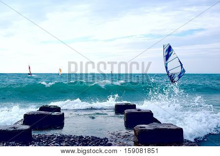 Group of windsurfers on boards in wavy sea with pier on coast. Lifestyle and sport completition concept. Group of people. Fun and leisure activity.