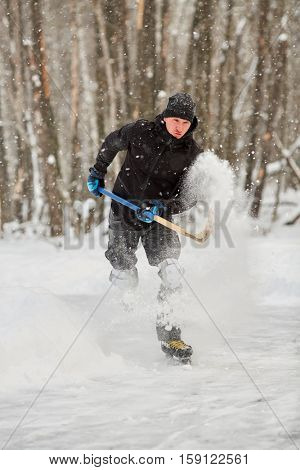 Hockey player runs throwing up puck and snow at outdoor skating rink in park.