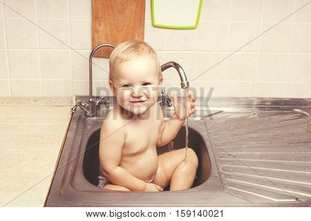Baby girl sitting in the kitchen sink. She is laughing
