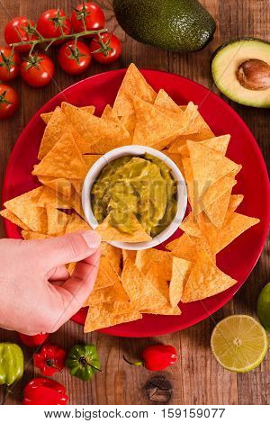 Guacamole and nacho chips on red dish.