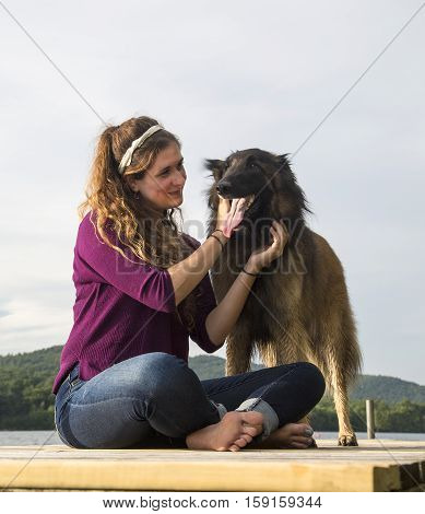 Young woman smiling at her dog on a dock at a lake