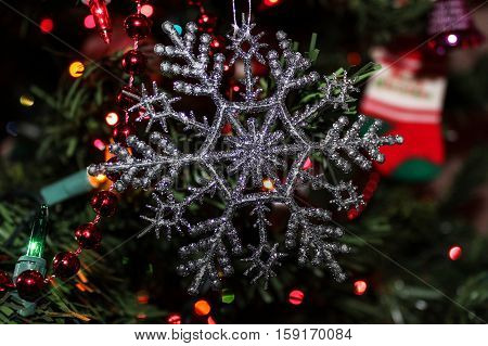 Close-up view of a festive silver glitter Christmas ornament hanging on the tree for the holidays with red bead garland.