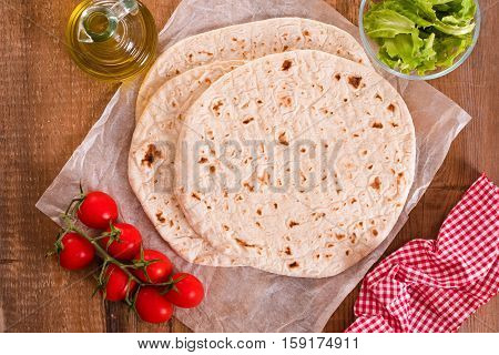 Piadina with ham and lettuce on wooden table.