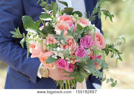 Beautiful bridal bouquet in hands of the groom. Wedding bouquet of peach roses  single-head pink rose aqua eucalyptus ruscus gypsophila