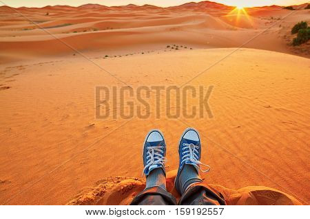 Feet of a woman relaxing on sand dunes and looking at sunrise in Sahara Desert Merzouga Morocco