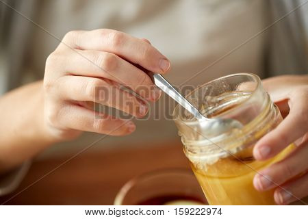 health, traditional medicine and ethnoscience concept - close up of woman hands with honey jar and spoon
