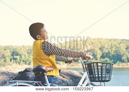 Asian boy with bicycle on the rock in river and blue sky backgroundvintage tone