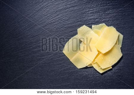 Top View Of Tasty Fresh Yellow Thin Slice Parm Cheese On Black Stone Slate Background, Close Up