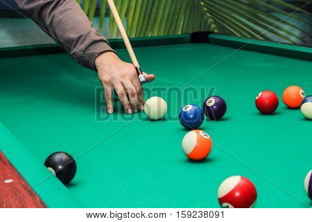 Billiard balls on green table and hand with billiard cue