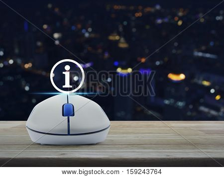 Wireless computer mouse with information sign icon on wooden table over blur light city tower