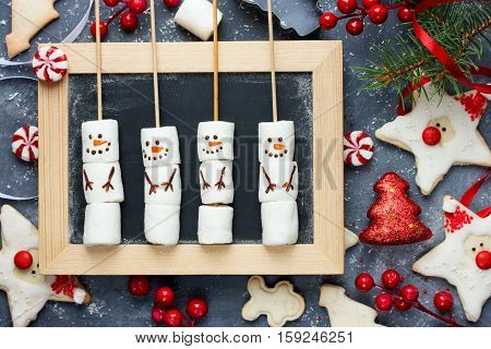 Christmas New Year treats for kids and holiday decorations funny Santa Claus and Christmas tree cookies with icing peppermint candy snowman marshmallow pops. Festive Christmas background