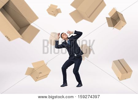 A frightened businessman and empty boxes falling on him, on the white background. Business loss. Crisis impact. Unsuccessful deal.