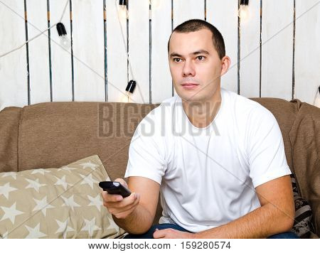 Young man sittting on the sofa with remote control and watching tv