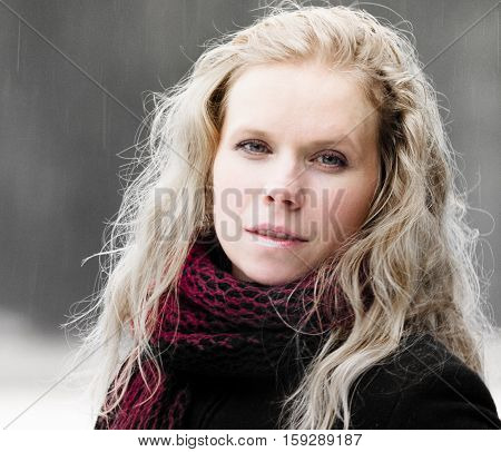 portrait of blond woman with blue eyes on a dark background winter girl in a black coat, curly hair, blond and beautiful, red scarf, light snow, cute look, half-smile, the kindness, photo on street,