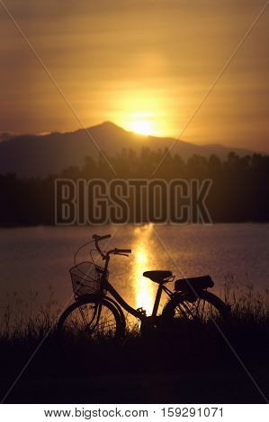 Retro Vintage Bicycle Near The Lake At Sunset Moment. Silhouette Bicycle At The Sunset With Grass Fi