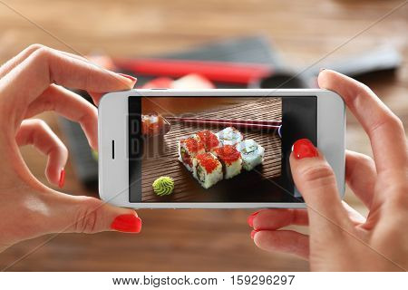 Woman taking photo of tasty sushi set