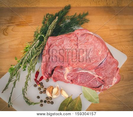Fresh raw beef on wooden cutting board, spices and herbs. Whole uncooked beef prepare for cooking. Large piece of fresh beef ham.