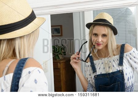 portrait of beautiful blond woman posing with summer hat in the mirror