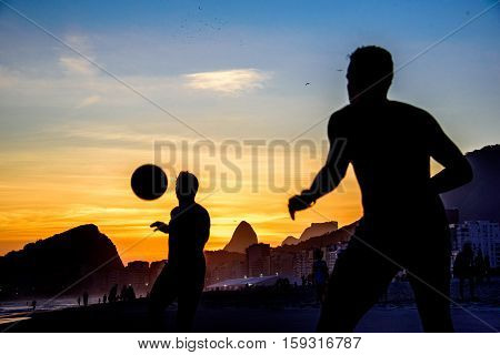 Beautiful sunset and silhouettes of men playing dar toques na bola game at Copacabana beach, Rio de Janeiro, Brazil