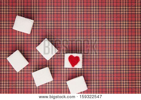 Sugar cubes with a red heart on one of them as background. Top view. Diet unhealty sweet addiction concept