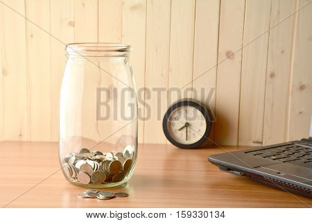 The coin inside of bottle ,alarm clock and lap top on the wood table.