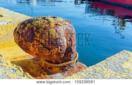 Rusty bitt in harbor with rope around it