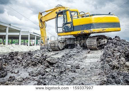 Yellow excavator is making pile of soil by pulling ground up on heap at construction site project in progress.