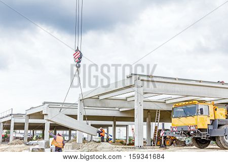 Workers are helping mobile crane to carry concrete joist for assembly huge construction.