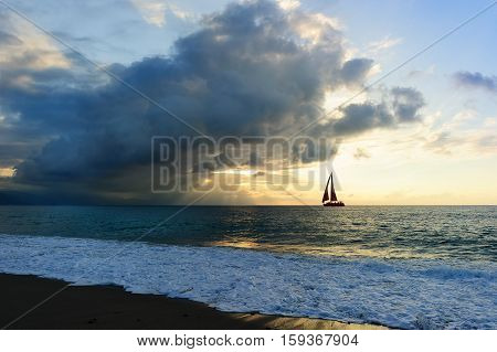 Ocean sunset sailboat sun ray silhouette is a bright uplifting seascape with sun beams breaking through the clouds as a sailboat is sailing along the ocean water..