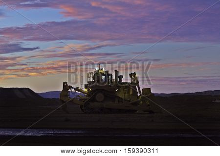 Yellow D11 bulldozer on a waste rock dump at sunrise at the Tom Price iron ore mine in the Pilbara region of Western Australia