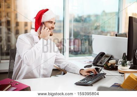 Young handsome businessman smiling speaking on phone at worplace in office on christmas day.