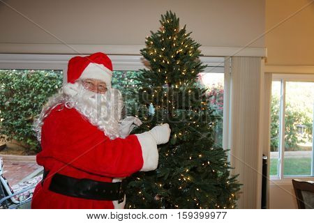 Santa Claus prepares a Christmas Tree with Lights and ornaments for Christmas at a persons house. Santa Loves xmas. x-masTree.   Santa Claus setting.