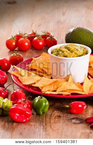 Guacamole and nacho chips on red dish.