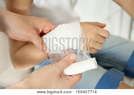 Woman wounding bandage around little boy's wrist, close up view