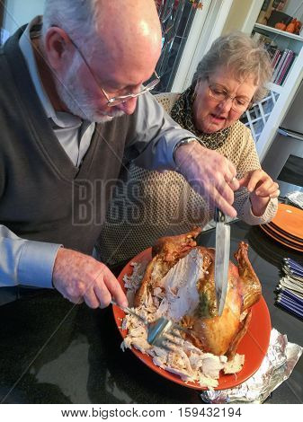 Senior Adult Couple Cutting the Holiday Turkey Together In The Kitchen.