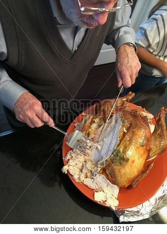 Senior Adult Man Cutting The Delicious Holiday Turkey in the Kitchen.
