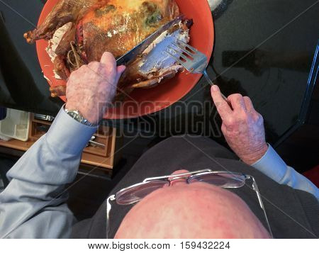 Senior Adult Man Cutting The Delicious Holiday Turkey in the Kitchen.