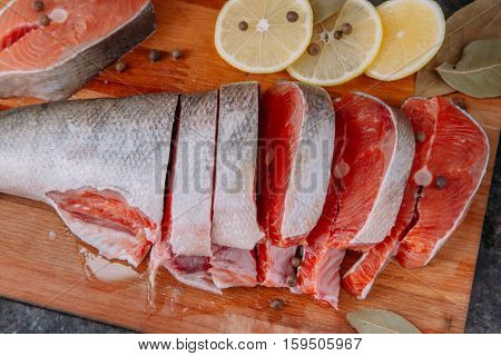 slices of raw salmon on a wooden board with lemon pepper and bay leaf