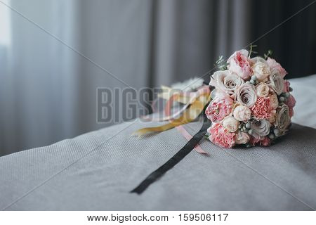 pink bridal bouquet with ribbons on the bed