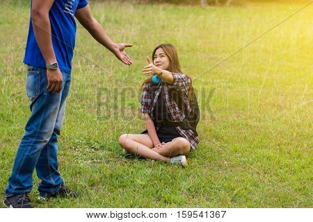 Woman sitting on the grass reaching to shake the hand of man. helping hand and love concept.