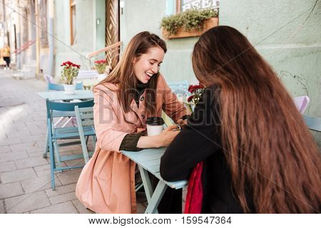Two cheerful cute young women drinking coffe and lauging in outdoor cafe
